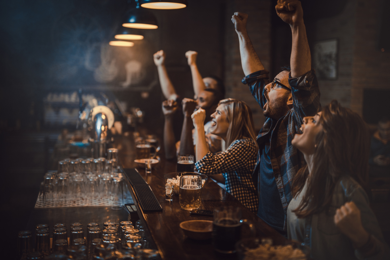 Large group of excited fans celebrating success of their sports team while watching a game in a bar.